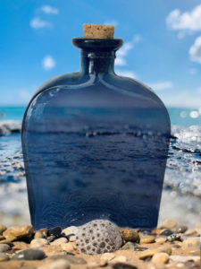 An antique blue water bottle on a beach